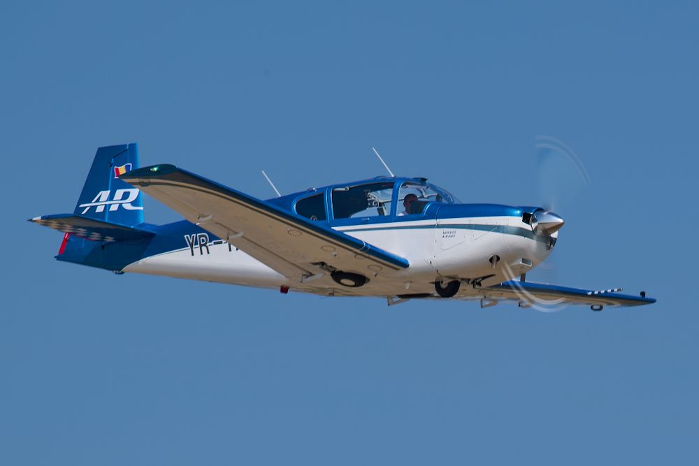 Blue and white private aircraft flying in clear daytime sky.