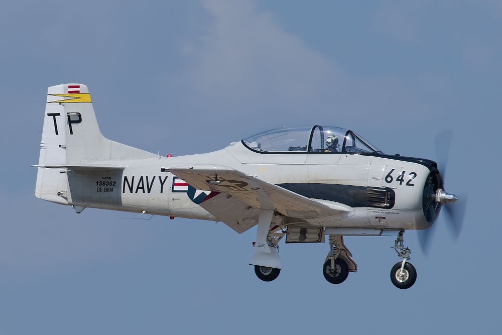 Classic T-28 Trojan military trainer aircraft in Navy colors flying against blue sky.
