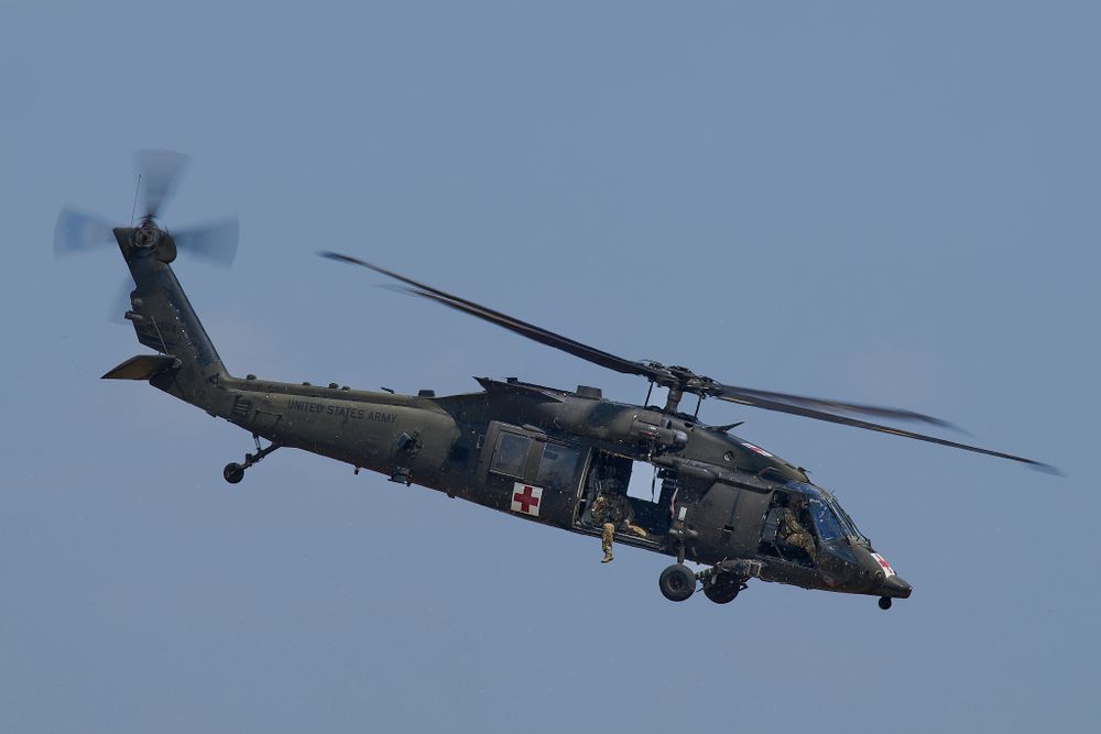 Military Blackhawk helicopter with rescue equipment flying in cloudy conditions.