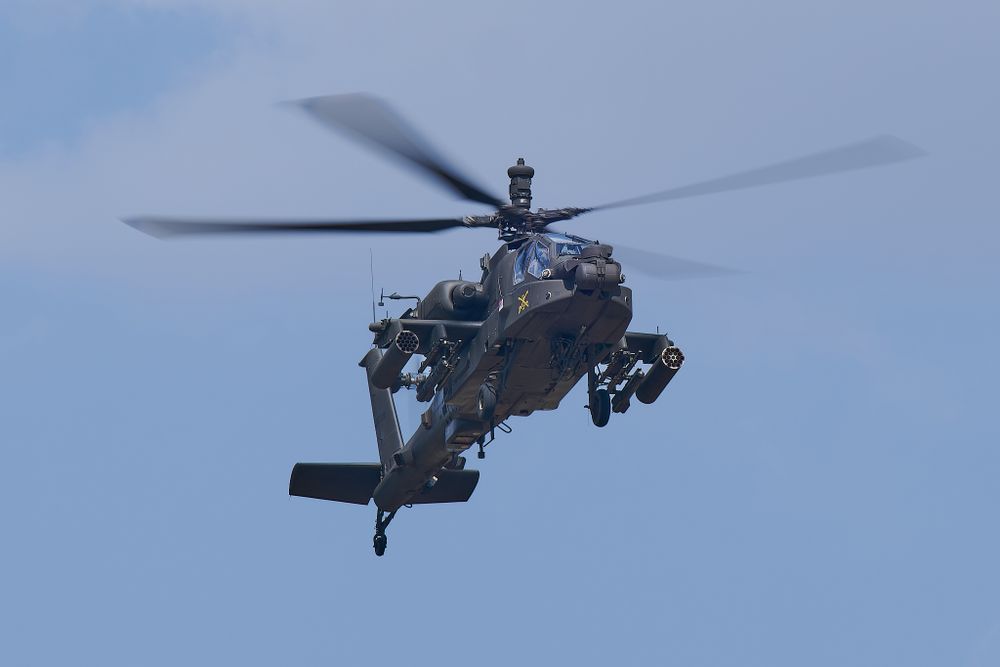 Apache attack helicopter performing aerial maneuver against blue sky background.