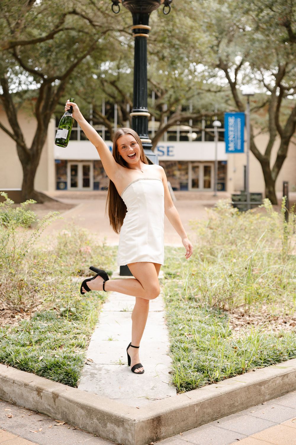 Joyful jumping poses on a concrete ledge surrounded by landscaping and campus buildings.