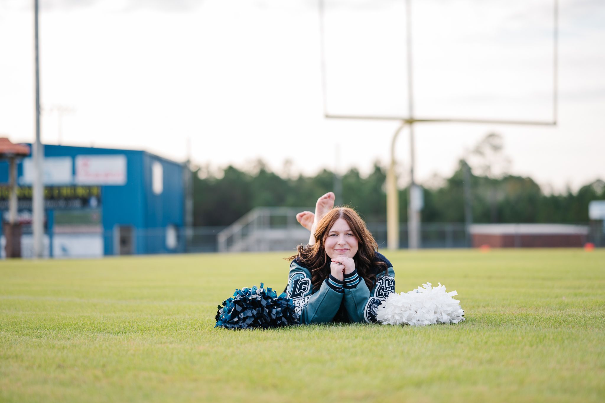 A cheerleader lying on a football field with blue and white pom poms.