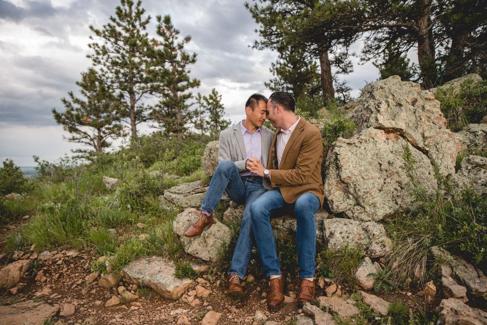 Couple sits close together on rocky mountain overlook.