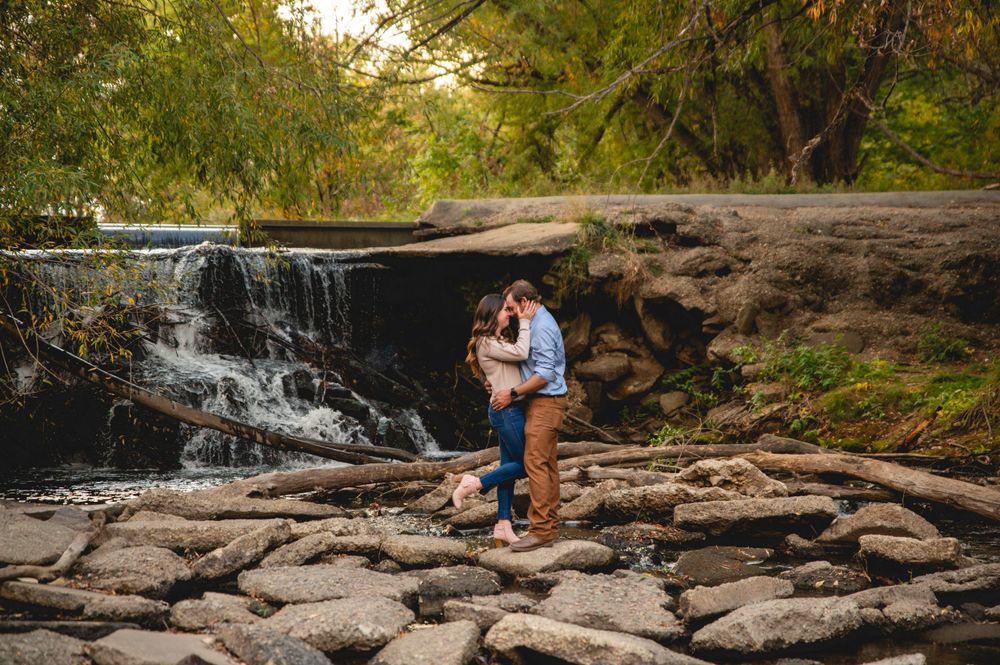 A romantic engagement photo of a couple embracing near a scenic waterfall.