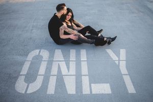 Couple sits together on pavement with ONLY text painted beneath them.