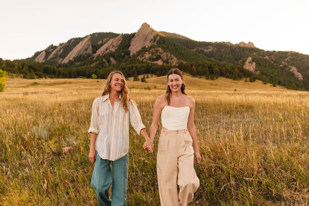 Couple standing in field at sunset with Flatirons rock formation in background.