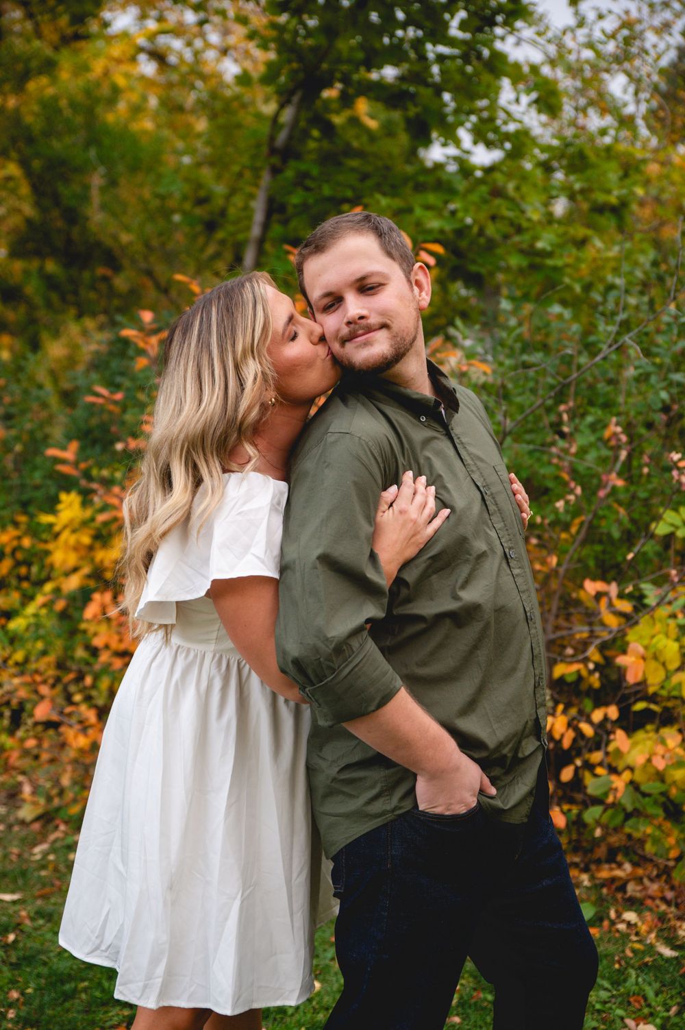 Romantic autumn engagement photo with couple embracing among colorful fall leaves.