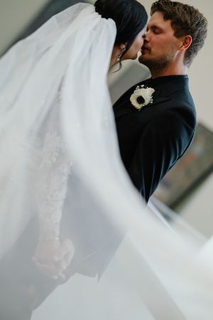 A romantic wedding photo series showing a couple embracing while a white veil flows in the wind.