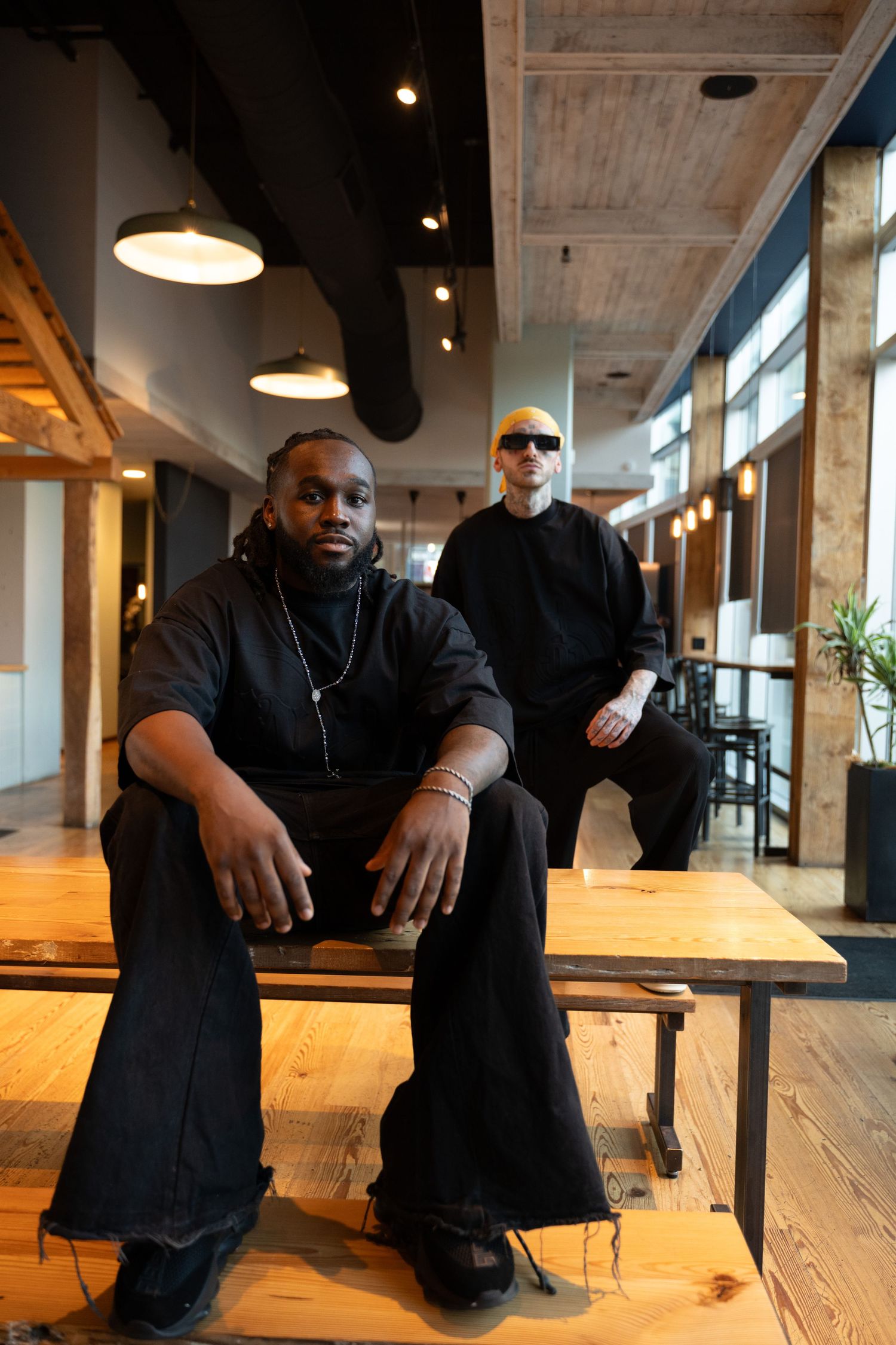Pixs By Tina captures two models in black clothing, one siting on a wooden bench other standing behind in an industrial styled area