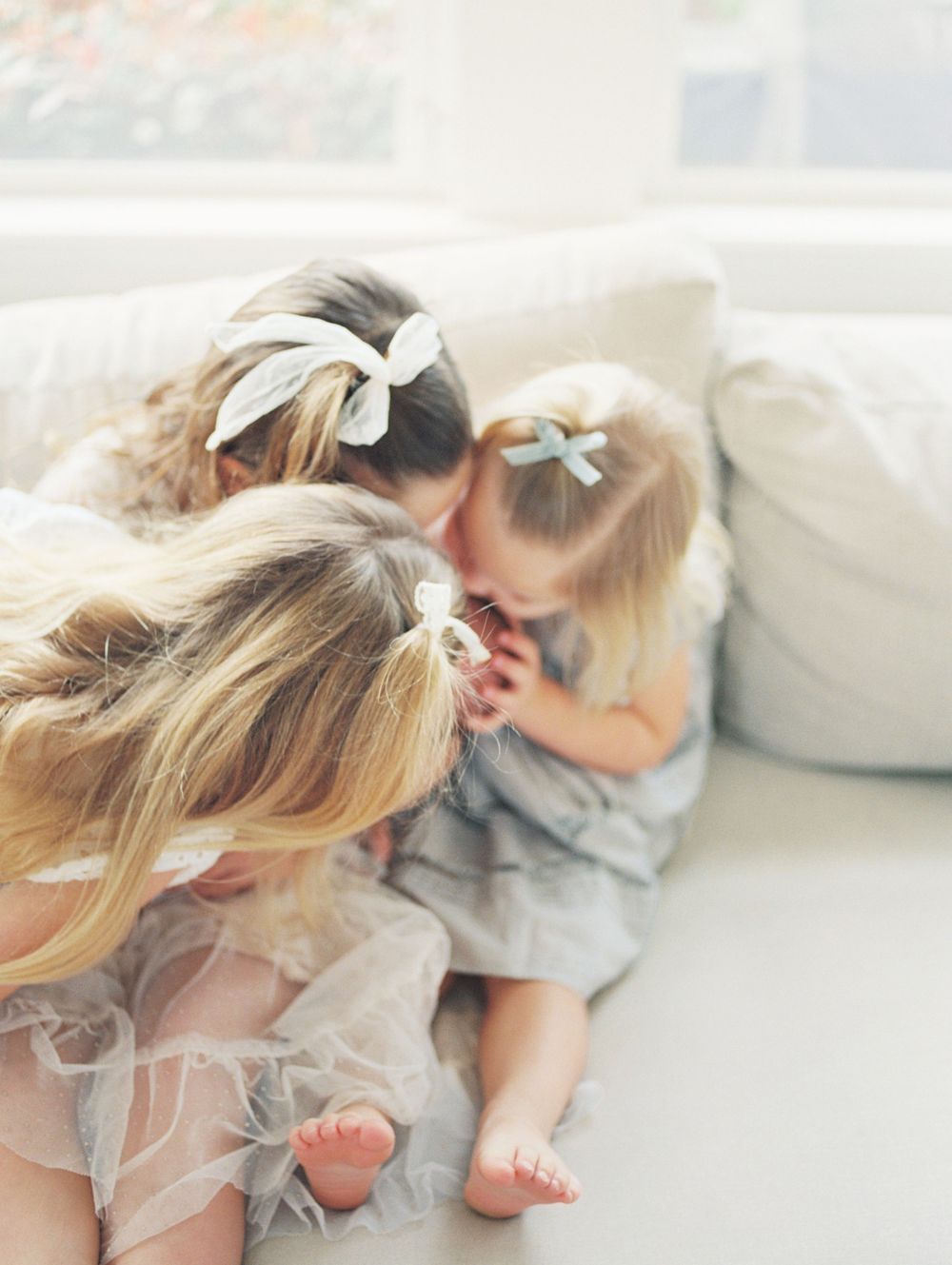 A series of dreamy, soft-focus photos showing a child in a light dress lying on white bedding in natural light.