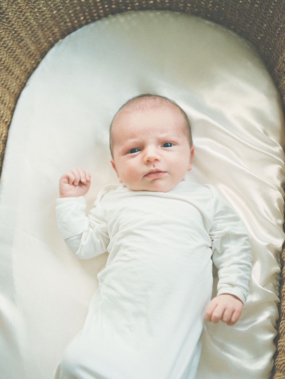 A small baby wearing white clothing lies on a soft cream-colored satin blanket in a series of connected photos.