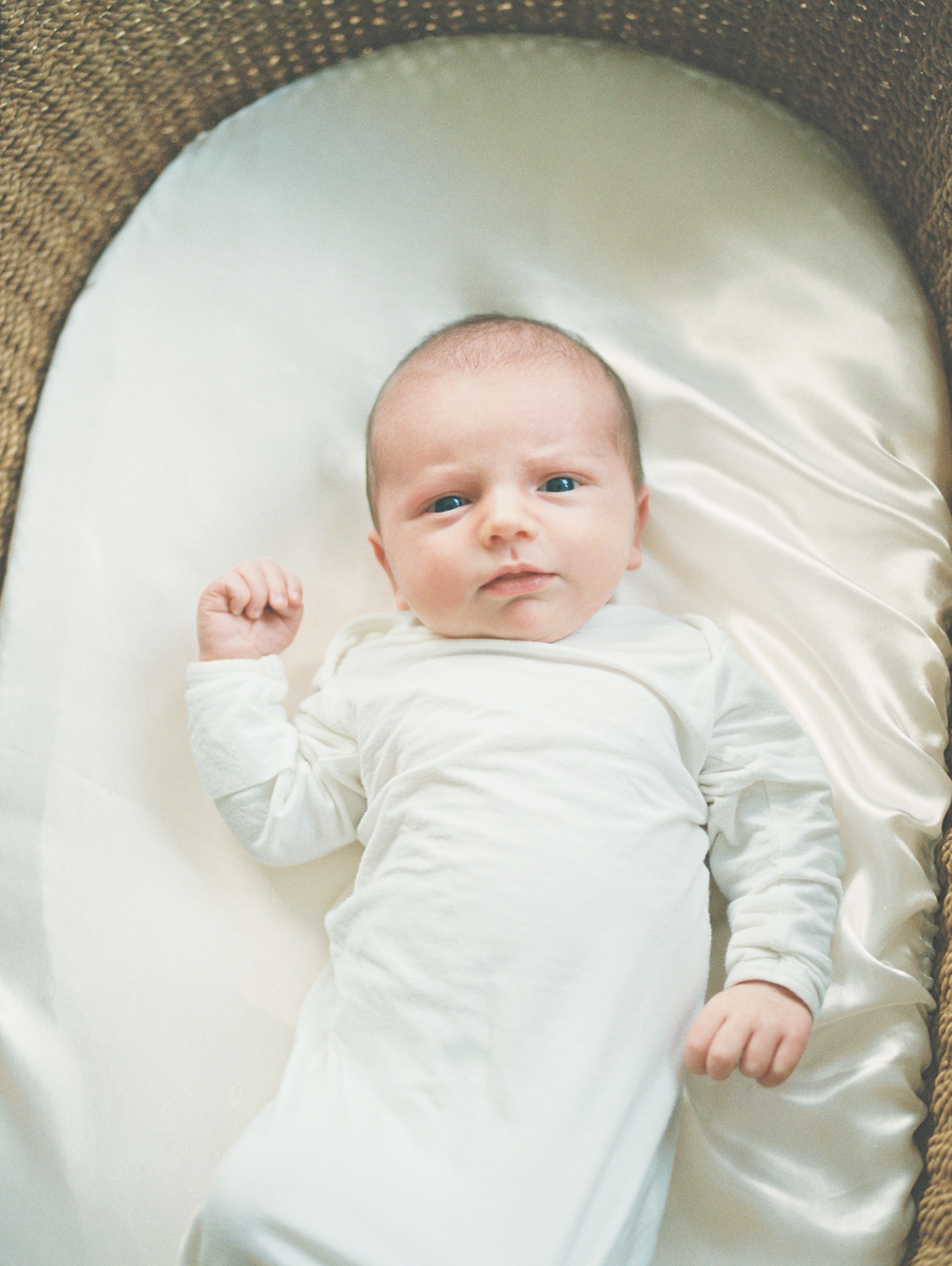 A small baby wearing white clothing lies on a soft cream-colored satin blanket in a series of connected photos.