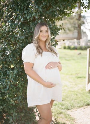 A person in a white top poses outdoors near green foliage in a sunlit garden setting.Film by Chelsee Rawe Photography