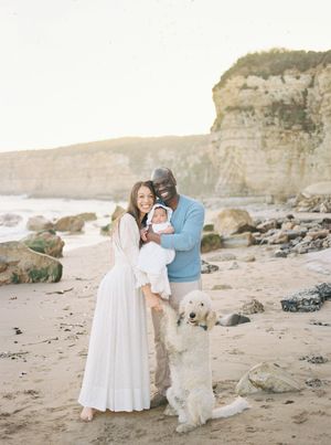 A family stands together on a scenic beach with towering cliffs in the background during sunset film by Chelsee Rawe Photography..