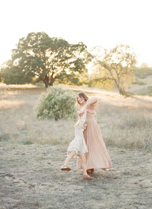A mother and child share a tender moment dancing together in a golden sunlit field at sunset among trees.By Chelsee Rawe Photography.