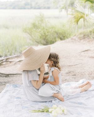 Mother in a sun hat with her little girl sitting on her lap on a blanket in a historic park captured by Chelsee Rawe