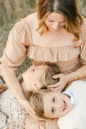 A tender family moment captured outdoors with soft lighting as they embrace and smile while lying on a floral blanket.By Chelsee Rawe Photog