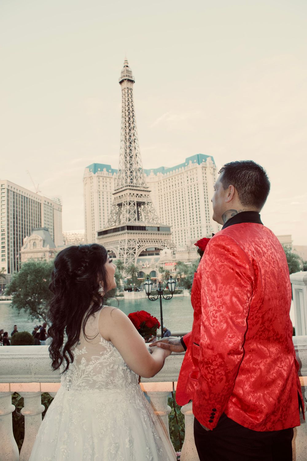 Bride and groom in red jacket hold hands overlooking Bellagio fountains and Paris Las Vegas tower.