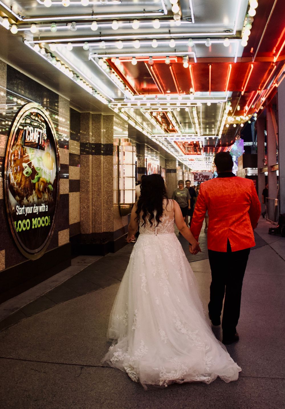 Newlyweds walk hand in hand through neon-lit Fremont Street Experience in Las Vegas on wedding night.