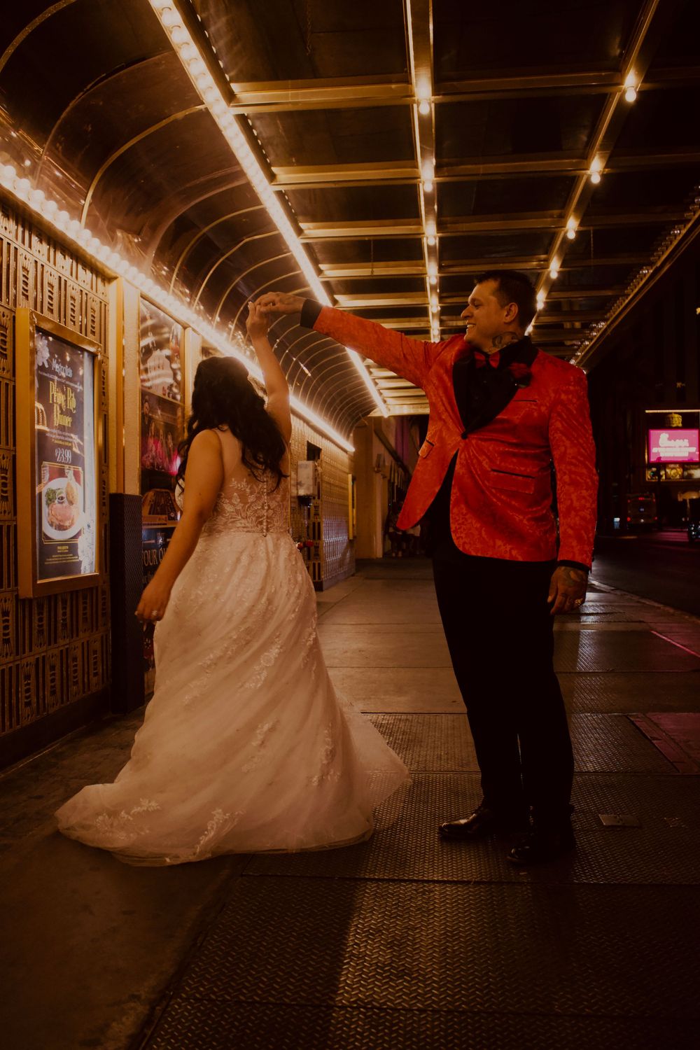 Bride and groom dancing under glowing lights on Las Vegas Strip at night, groom in red jacket twirling bride in white gown.