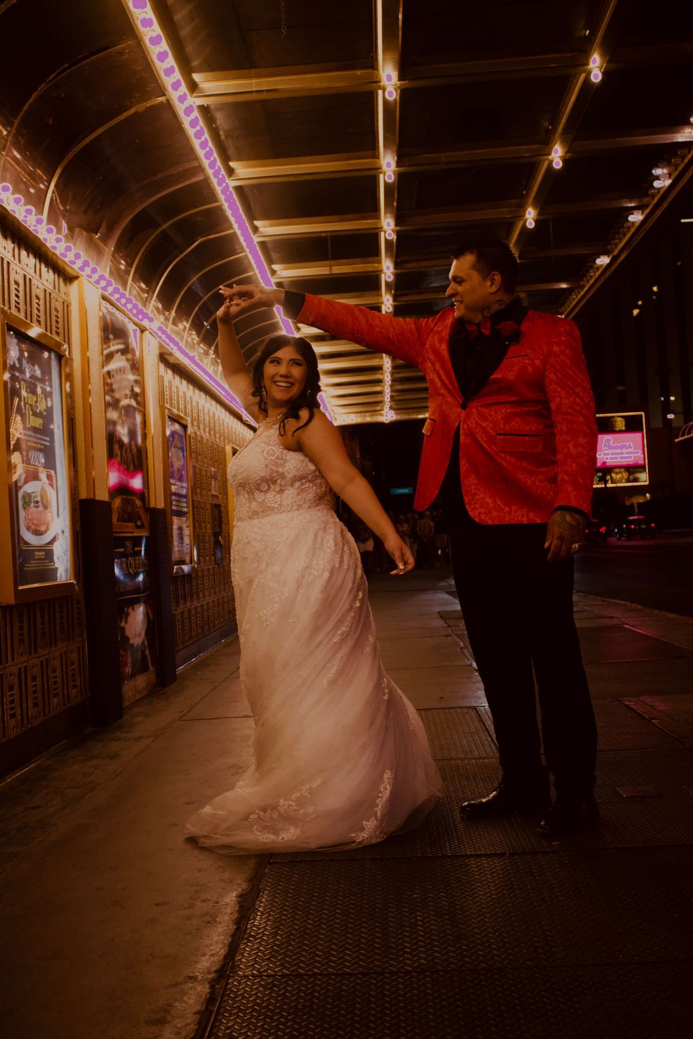 Bride and groom dancing under glowing arcade lights on the Las Vegas Strip at night.