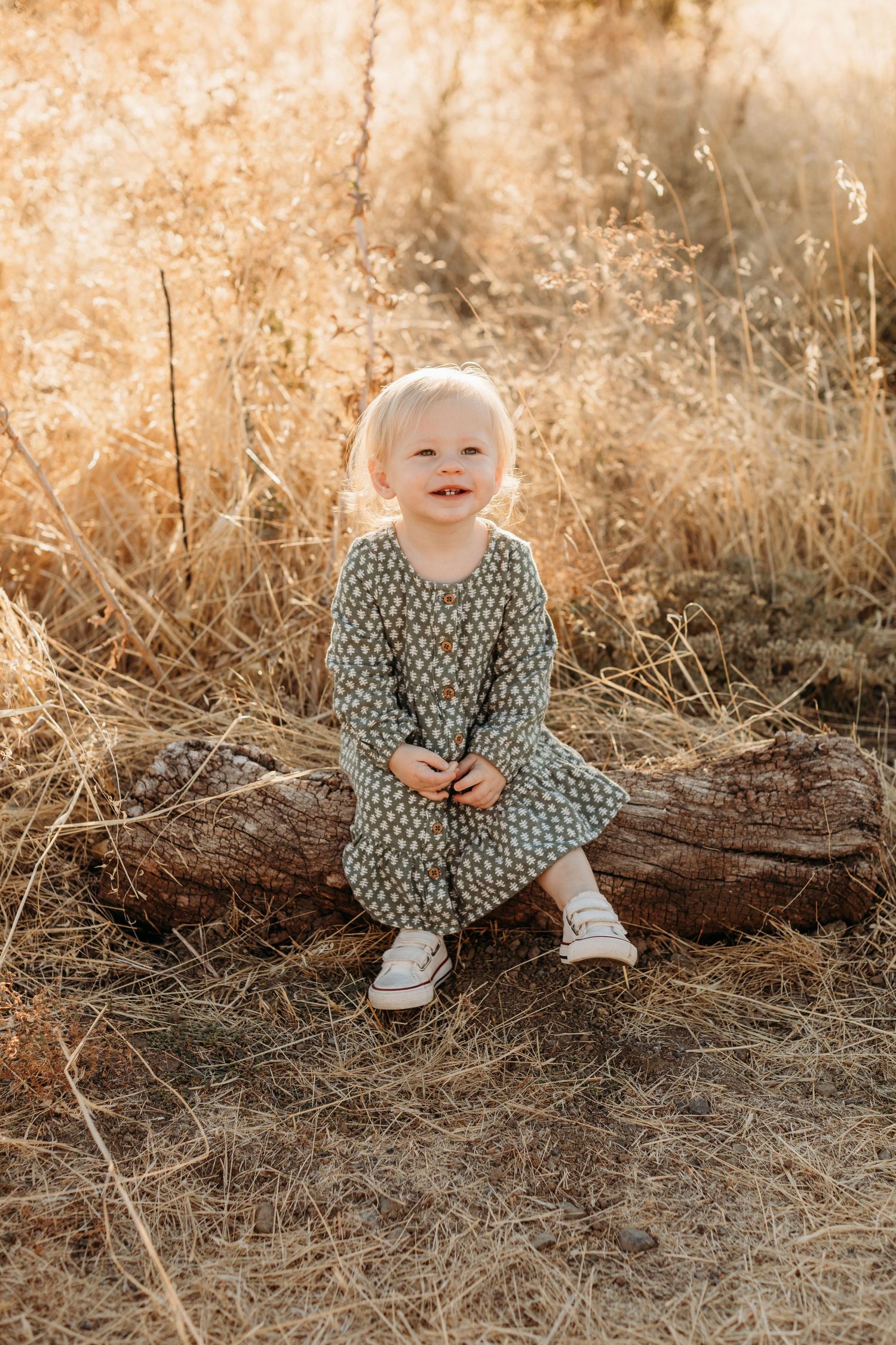 Young child in polka dot dress sitting on log during golden hour.