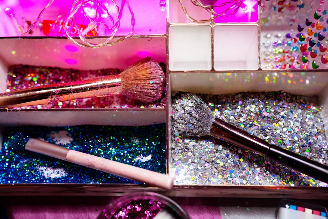 Colorful craft supplies and glitter organized in pink compartment storage box.