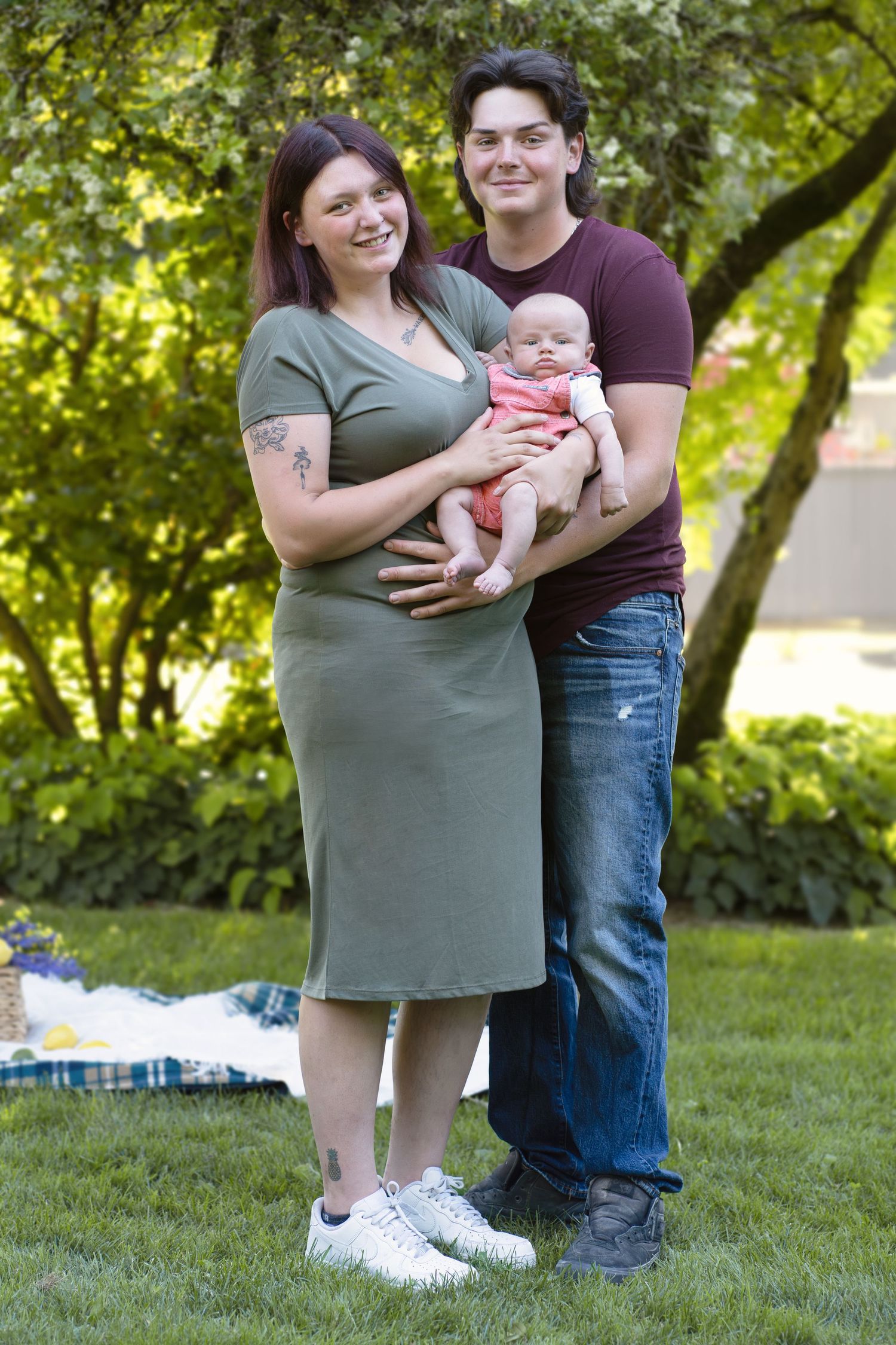 A family standing together on grass with leafy green trees creating a natural backdrop.