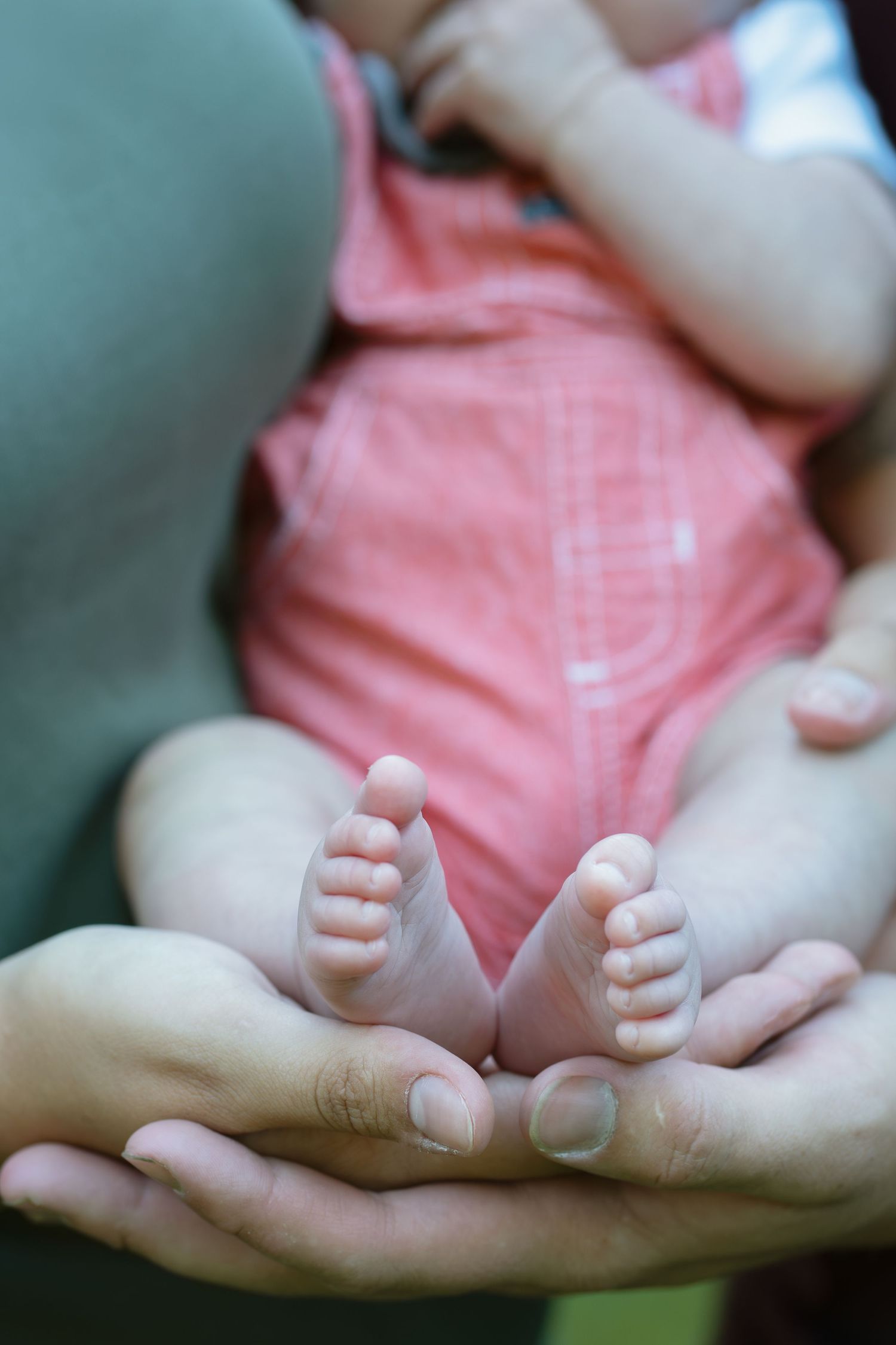 Tiny newborn baby feet resting in gentle hands against a pink background.