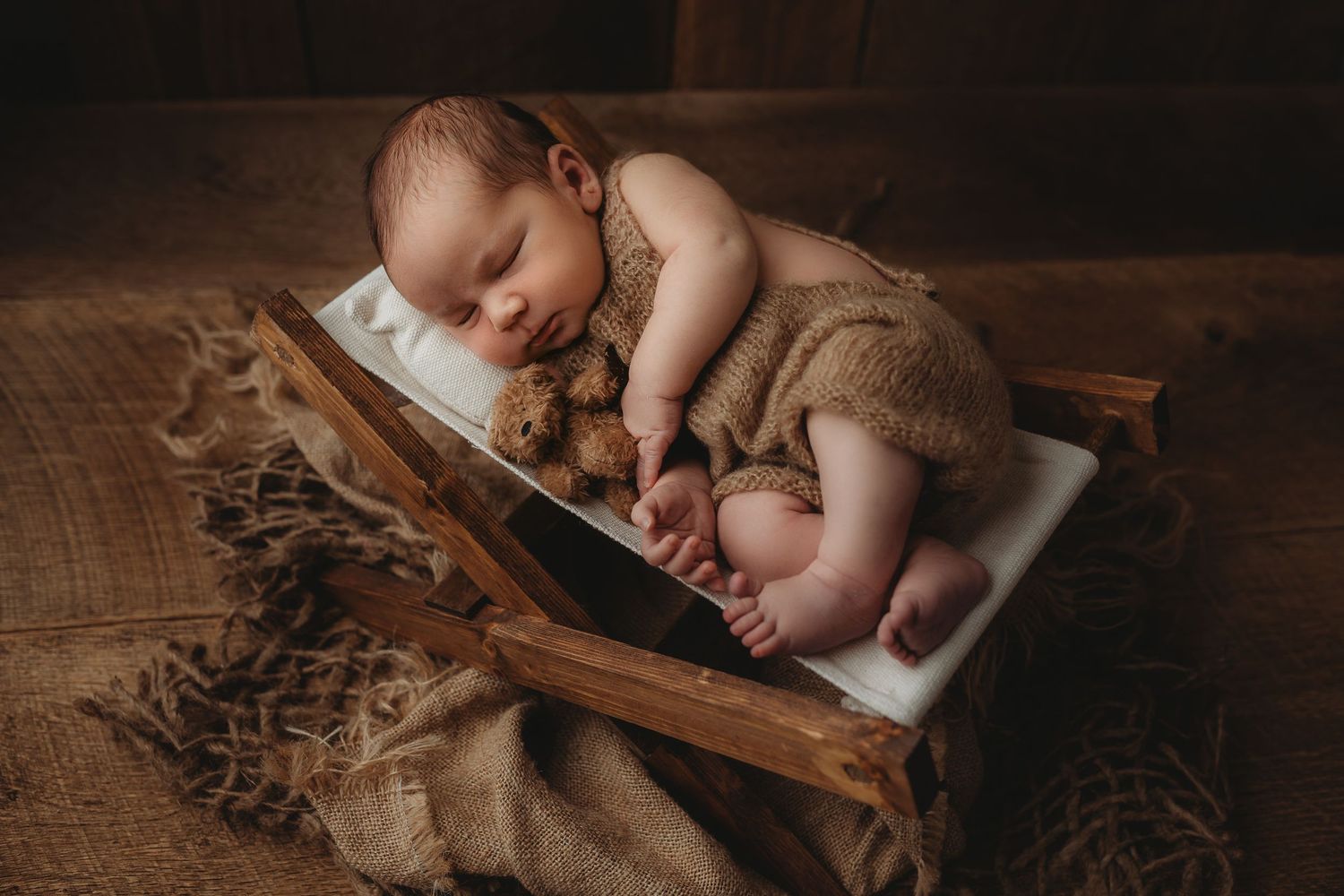 Sleeping newborn baby wrapped in brown knit blanket against dark background in artistic portrait.
