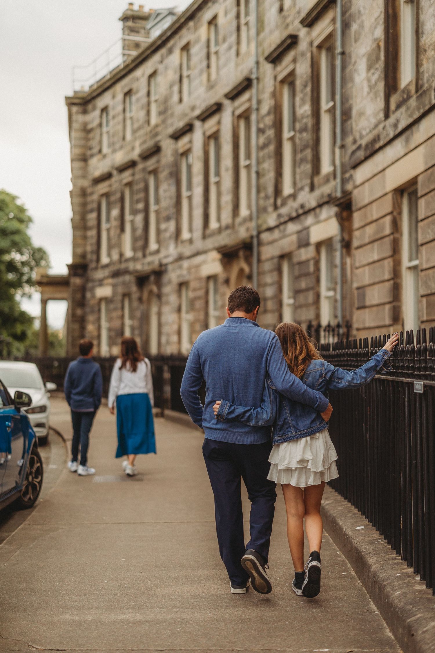 A couple walking arm in arm down a historic Edinburgh street with classic architecture.