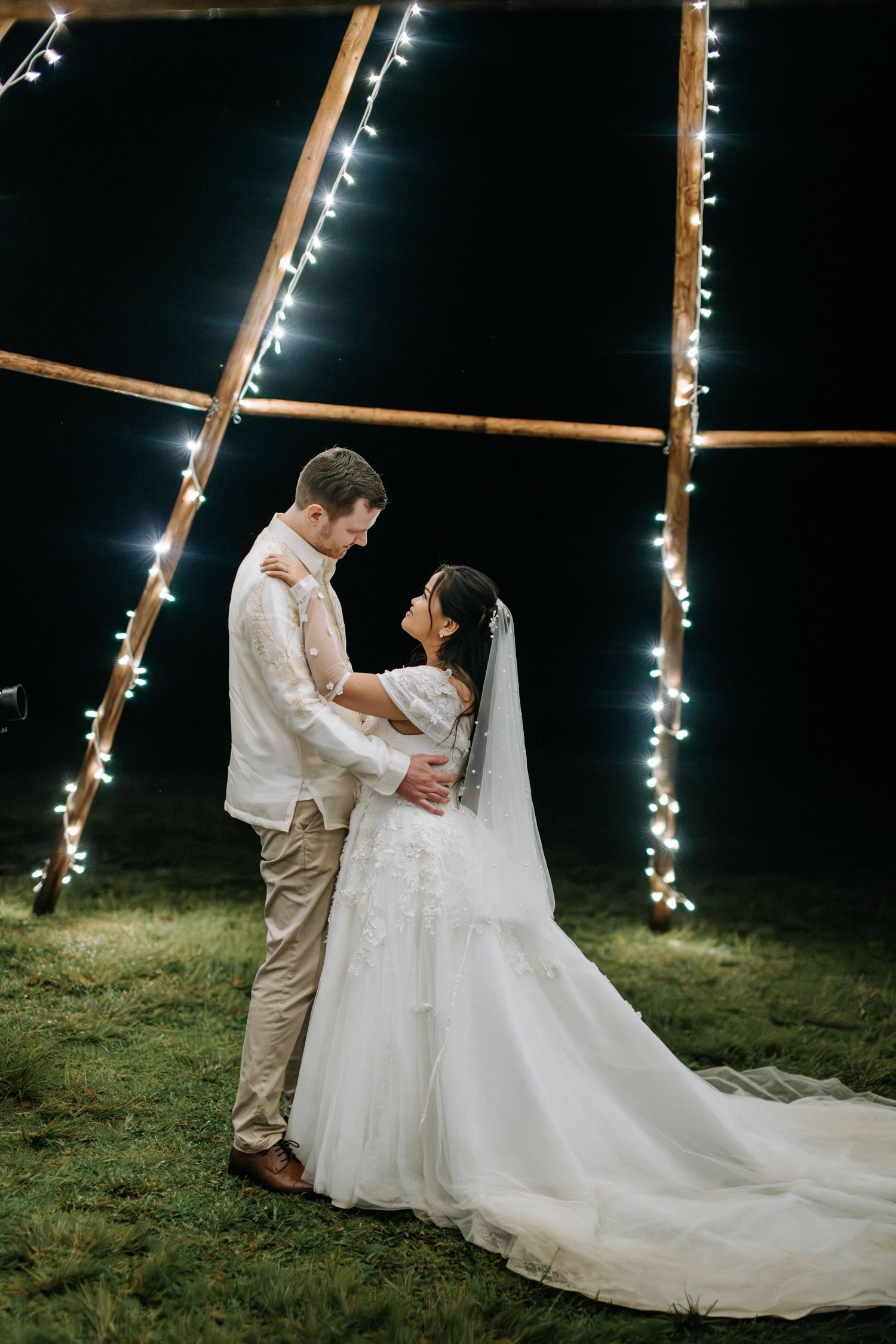 Romantic nighttime wedding portrait under string lights and tent structure.