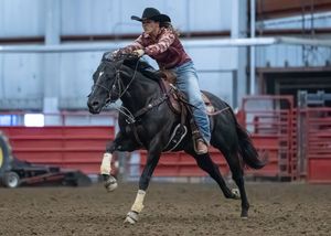 A cowboy rider bucks on a black horse during a rodeo bronc riding competition in an arena.