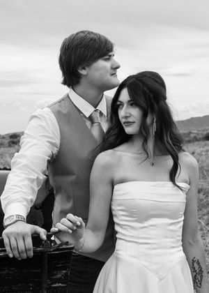Black and white wedding photo of a young couple, bride in strapless gown, groom in vest and tie, outdoors.