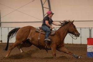Horse and rider racing past barrels in an indoor rodeo arena during barrel racing competition.