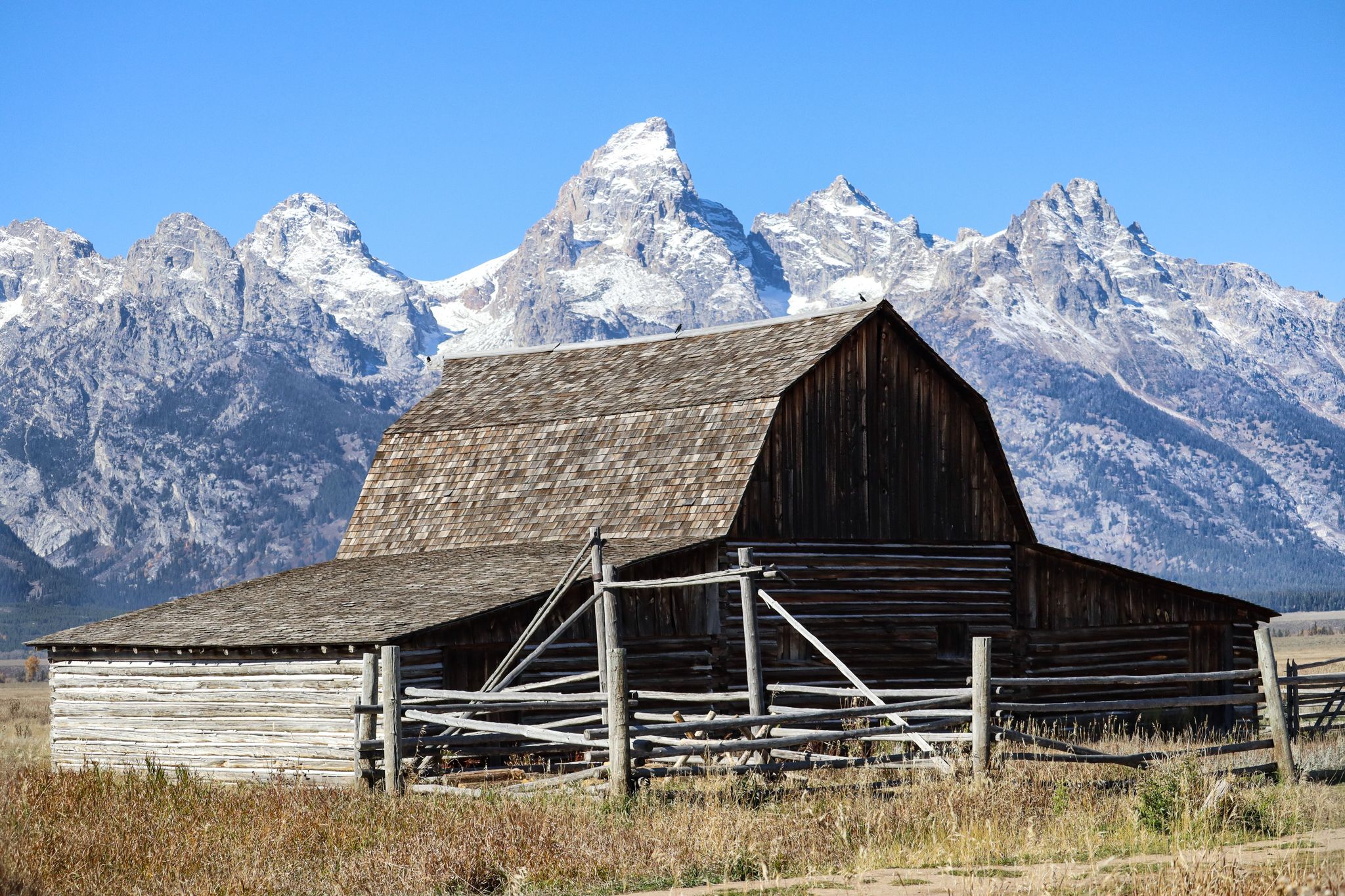 Rustic wooden barn with snow-capped Grand Teton mountains rising majestically in the background.