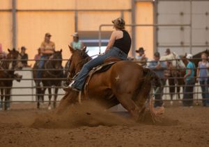 Horse and rider performing a tight turn during indoor barrel racing competition with spectators watching.