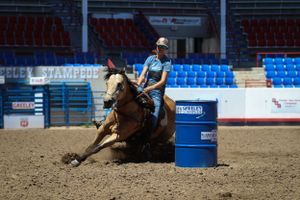 Equestrian athlete competing in barrel racing at a rodeo event with stadium seating visible.
