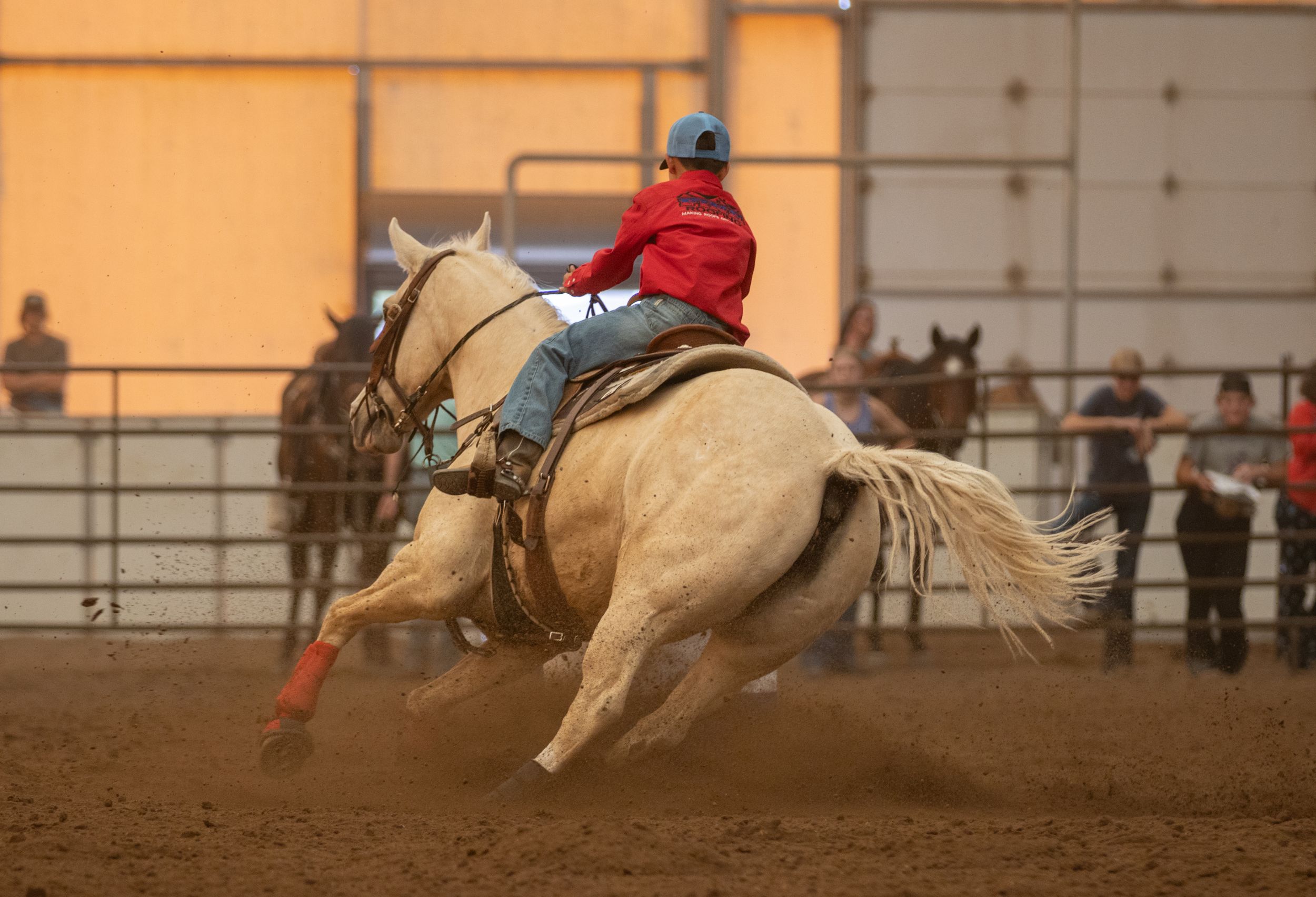 Palomino horse and rider competing in barrel racing at an indoor rodeo arena.