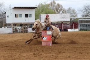 Equestrian athlete racing around a barrel in a dirt arena during competition.