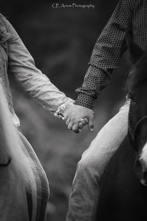 Black and white close-up of two people holding hands showing wedding rings.