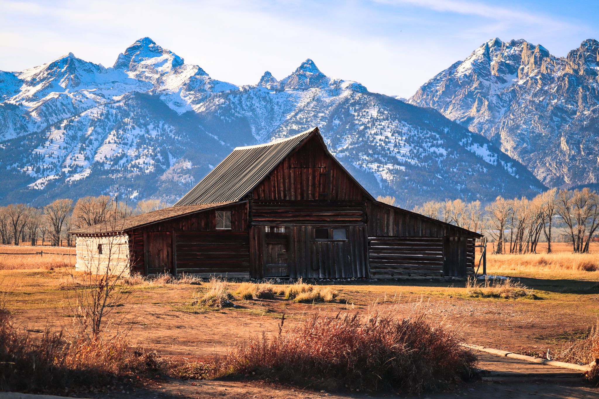 Rustic wooden barn against snow-capped mountain range in Grand Teton National Park.