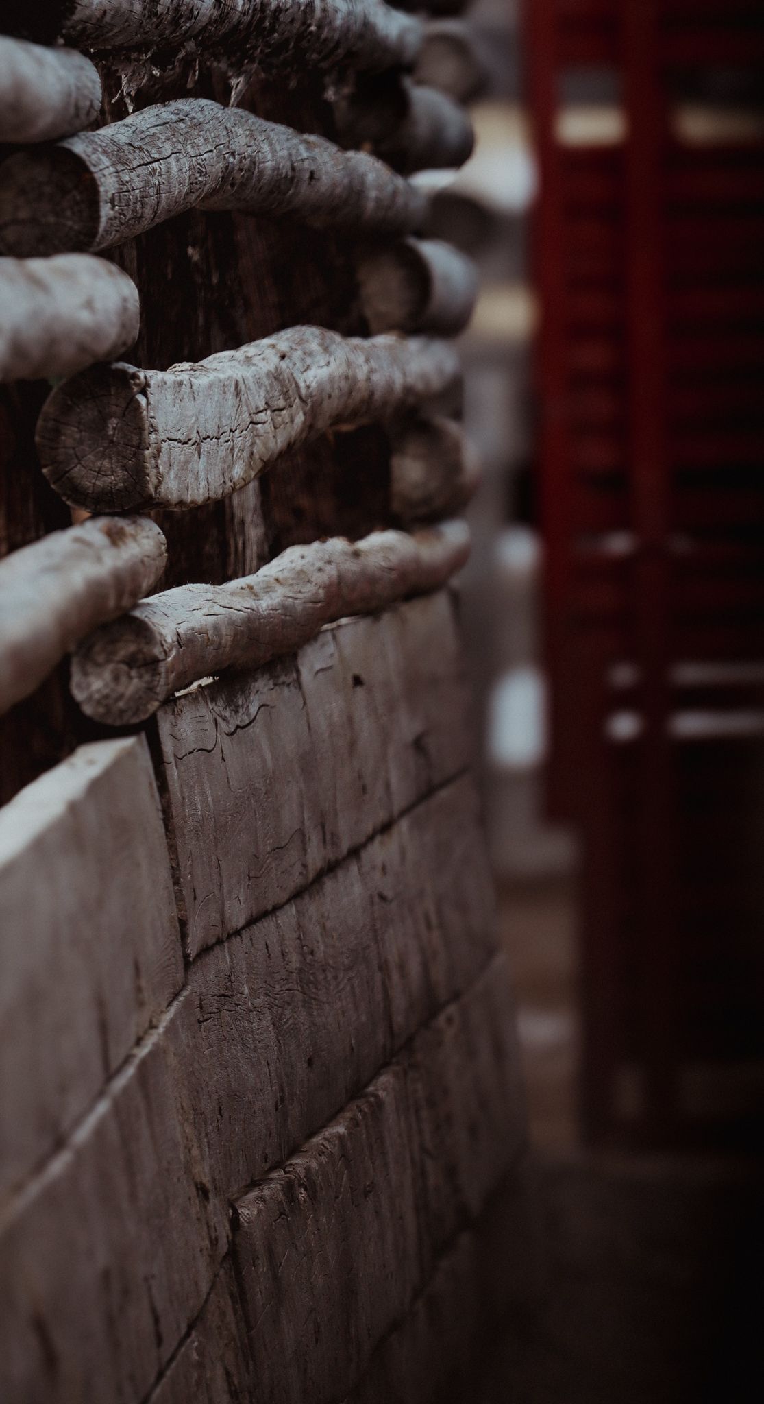 Close-up of stacked firewood logs creating textured pattern with red background.