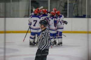 Hockey referee watches as team celebrates in background on ice rink.