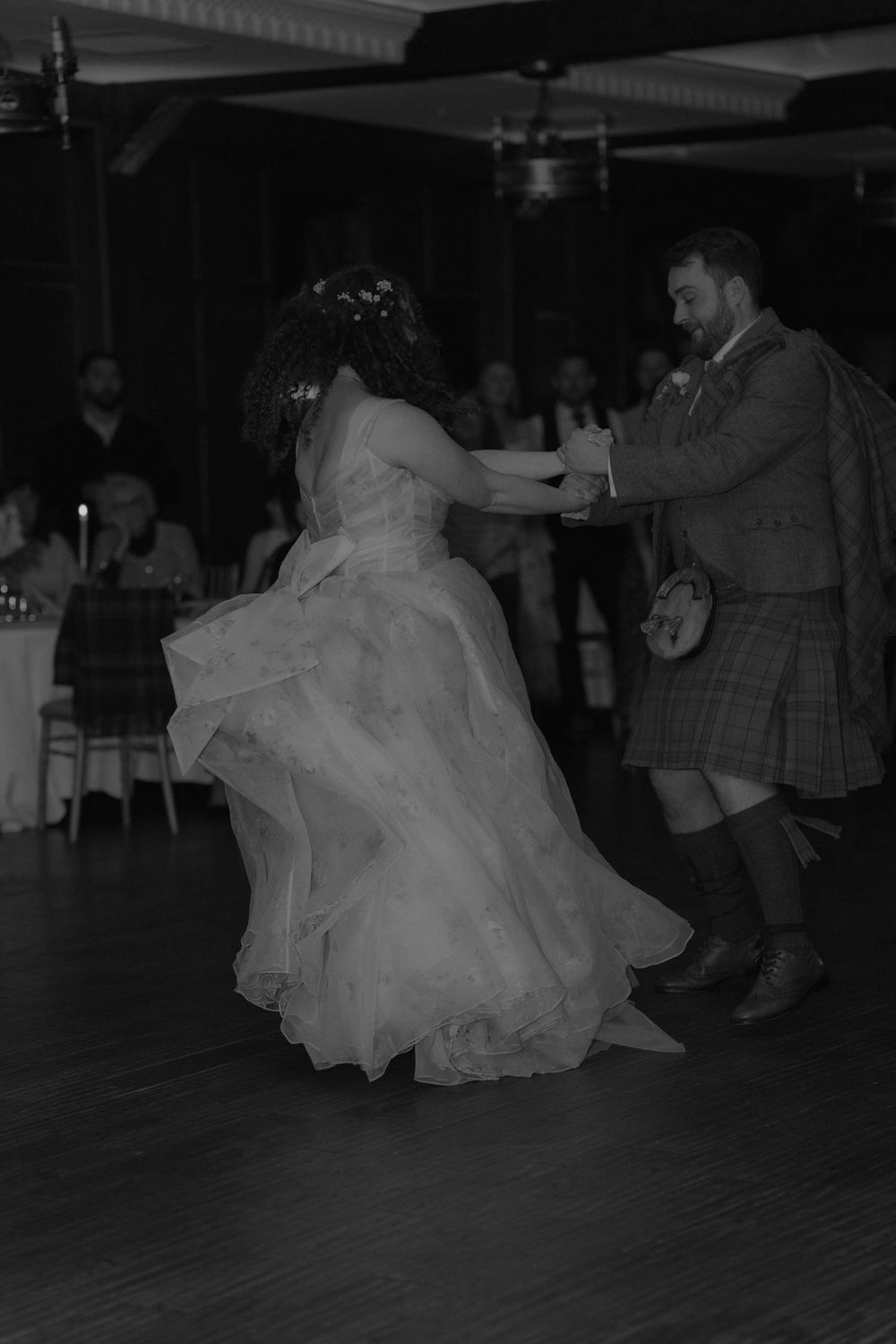 Bride and groom share a lively first dance, with her gown flowing as he wears a traditional Scottish kilt.