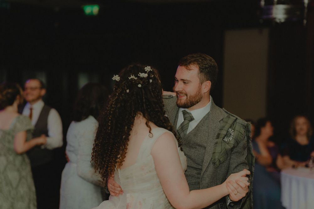 Bride and groom share their first dance, smiling warmly at each other in a softly lit wedding reception venue.