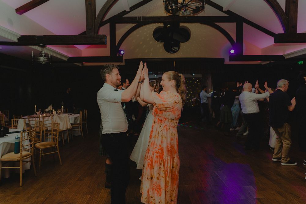 Couple high-fiving on wedding reception dance floor in rustic barn venue with warm lighting.