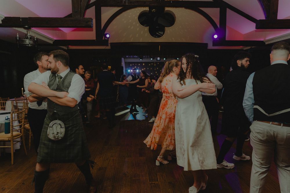 Couples dancing joyfully at a wedding reception in a rustic venue with warm lighting.