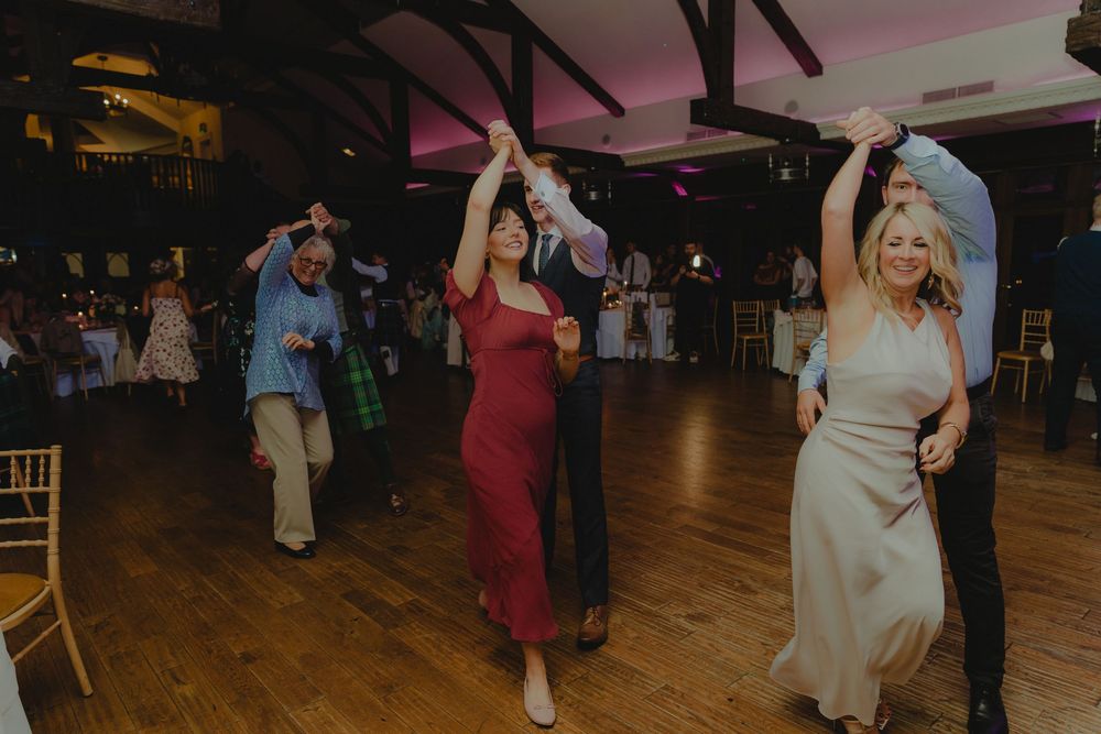 Guests dancing joyfully at a wedding reception on a wooden dance floor in an elegant venue.