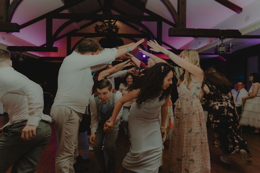Energetic wedding reception dance floor with guests celebrating under purple lights.